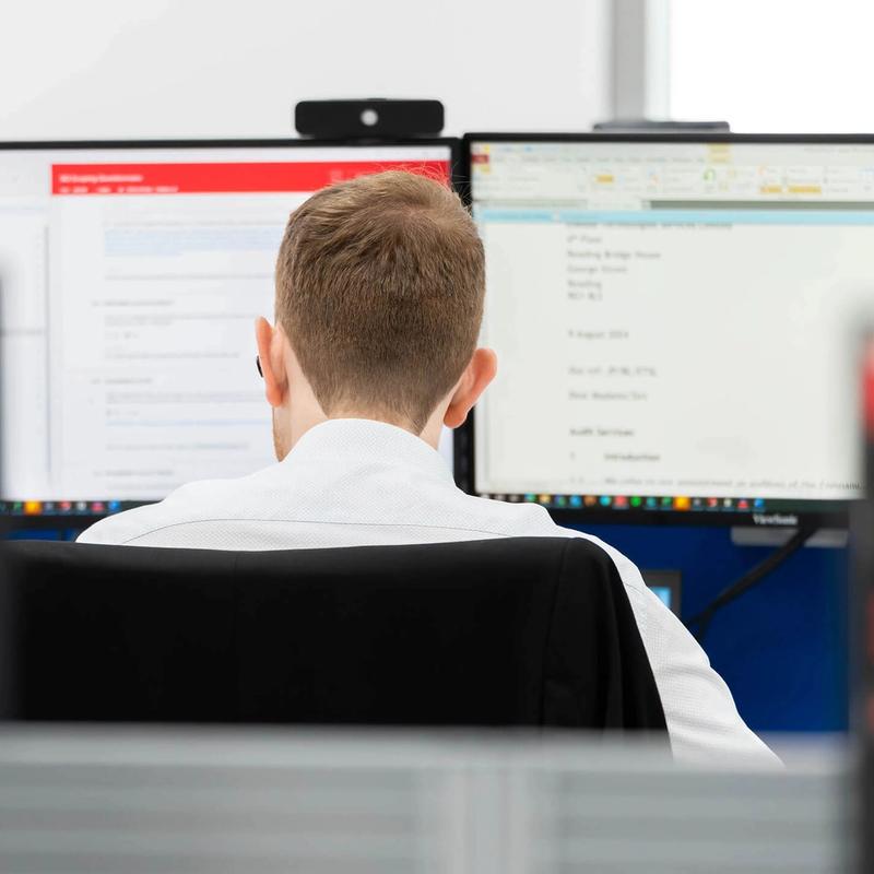 A C5 Team Member working on his laptop and additional monitors at his desk in the office