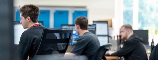 Several IT Services C5 Team Members working on their laptops and additional monitors at their desks in the office