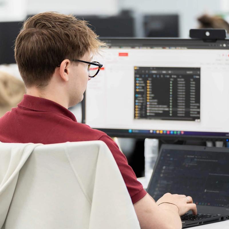 A C5 Team Member working on his laptop and additional monitors at his desk in the office
