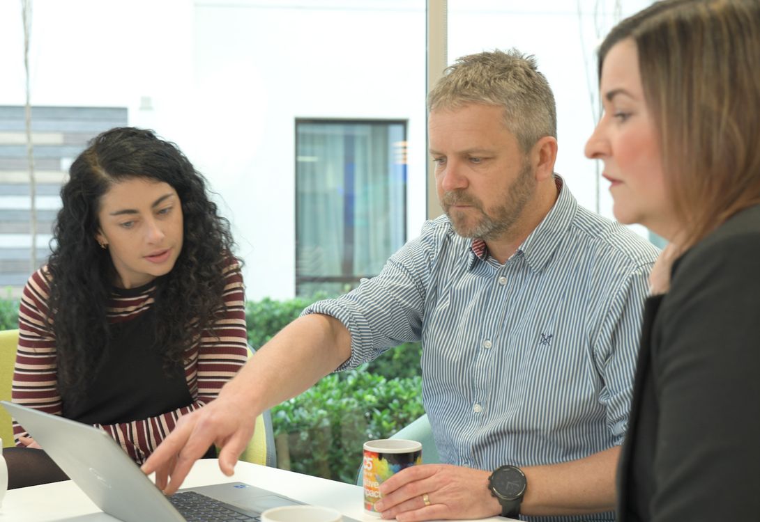A senior C5 team leader demonstrates a new app they have developed on a laptop computer while the clients watch and review